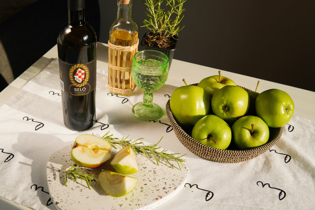A bowl of fresh apples next to a bowl of olives and a bottle of Croatian olive oil.