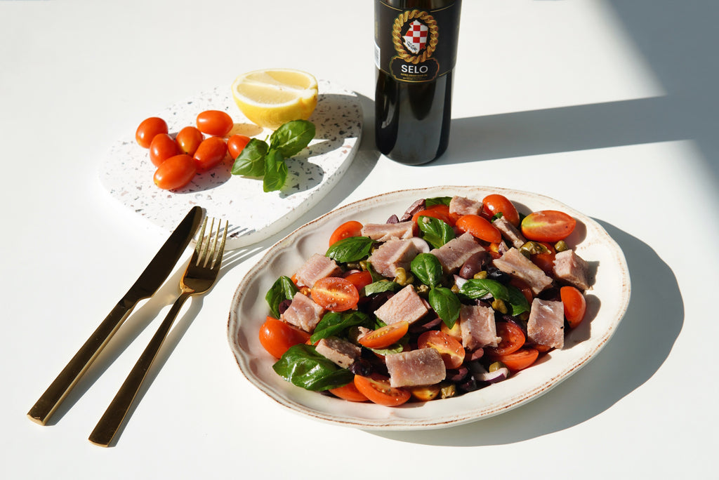 A vibrant Tuna on Olive and Tomato Salad served in a glass bowl, featuring colorful tomatoes, olives, and chunks of tuna.
